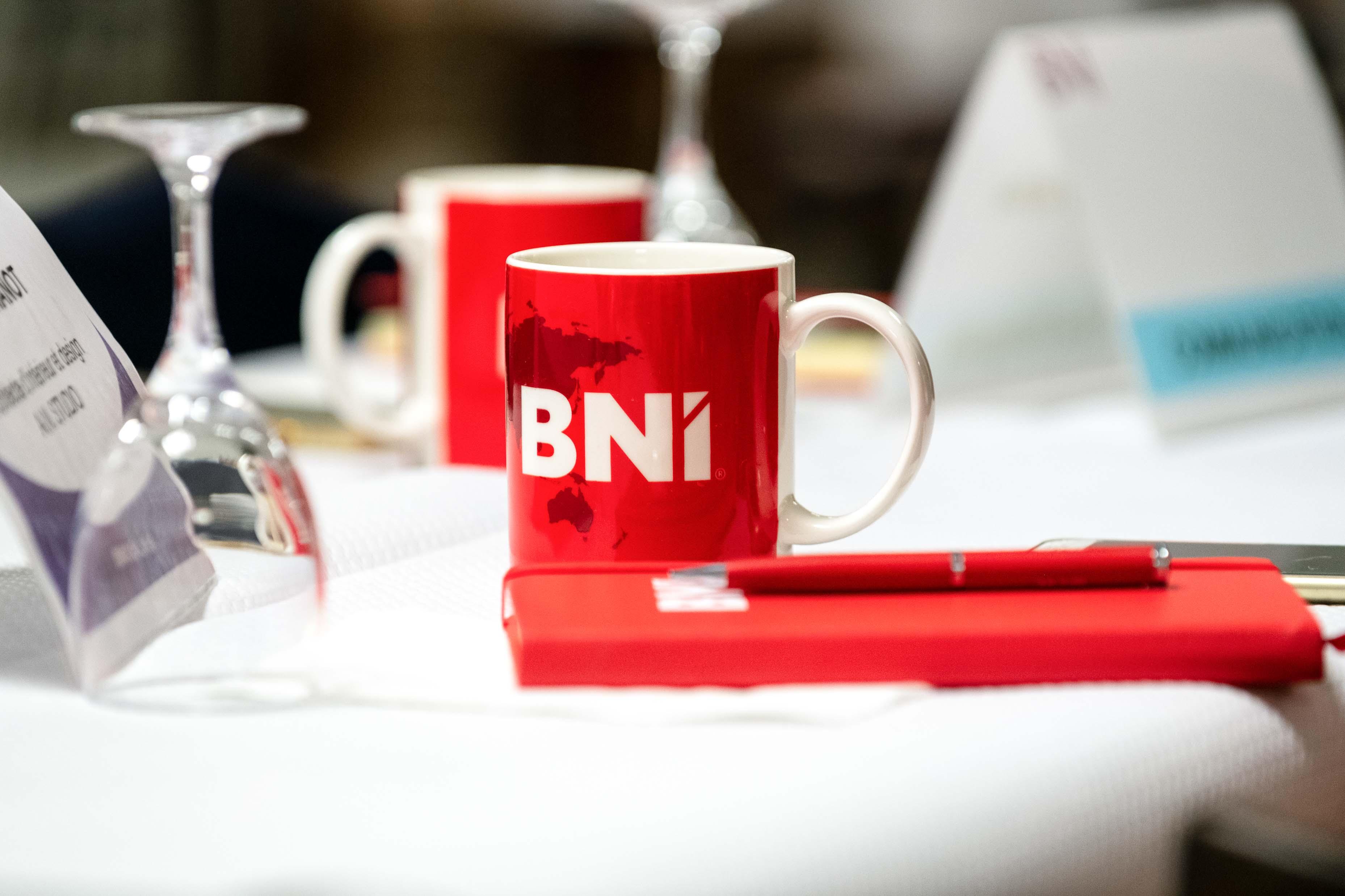 Tasse rouge BNI posée sur une table de réunion avec carnet et stylo assortis, lors d'un événement de networking professionnel